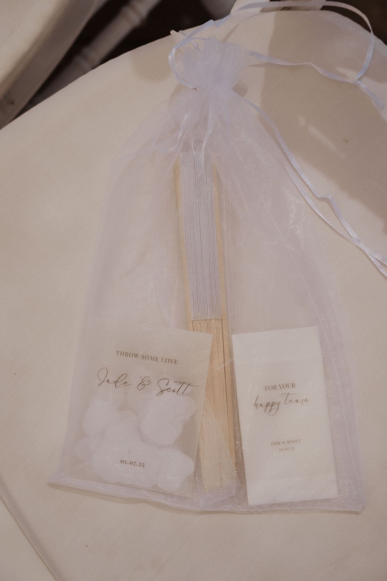 White sheer organza gift bags with elegant calligraphy tags displayed on a light neutral surface.