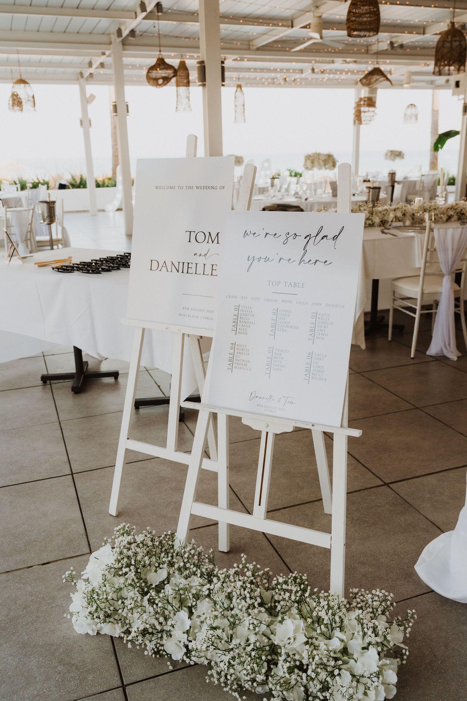Wedding seating chart displays on white easels decorated with baby's breath flowers at the base.