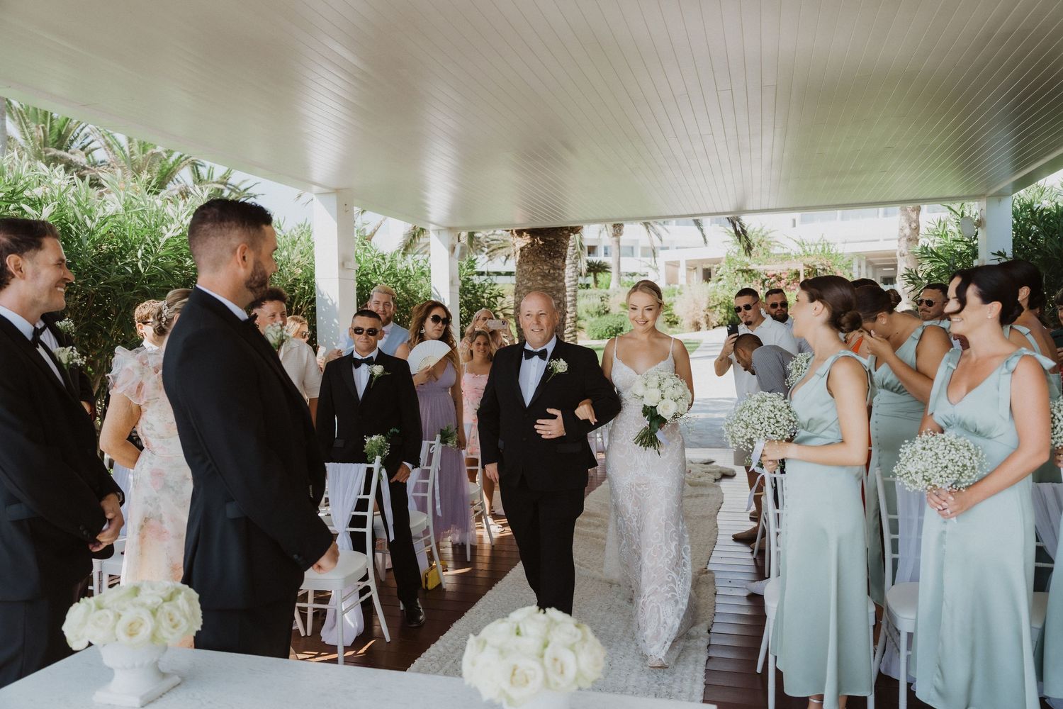 Wedding ceremony in a covered outdoor venue with light blue bridesmaid dresses and white floral decorations.
