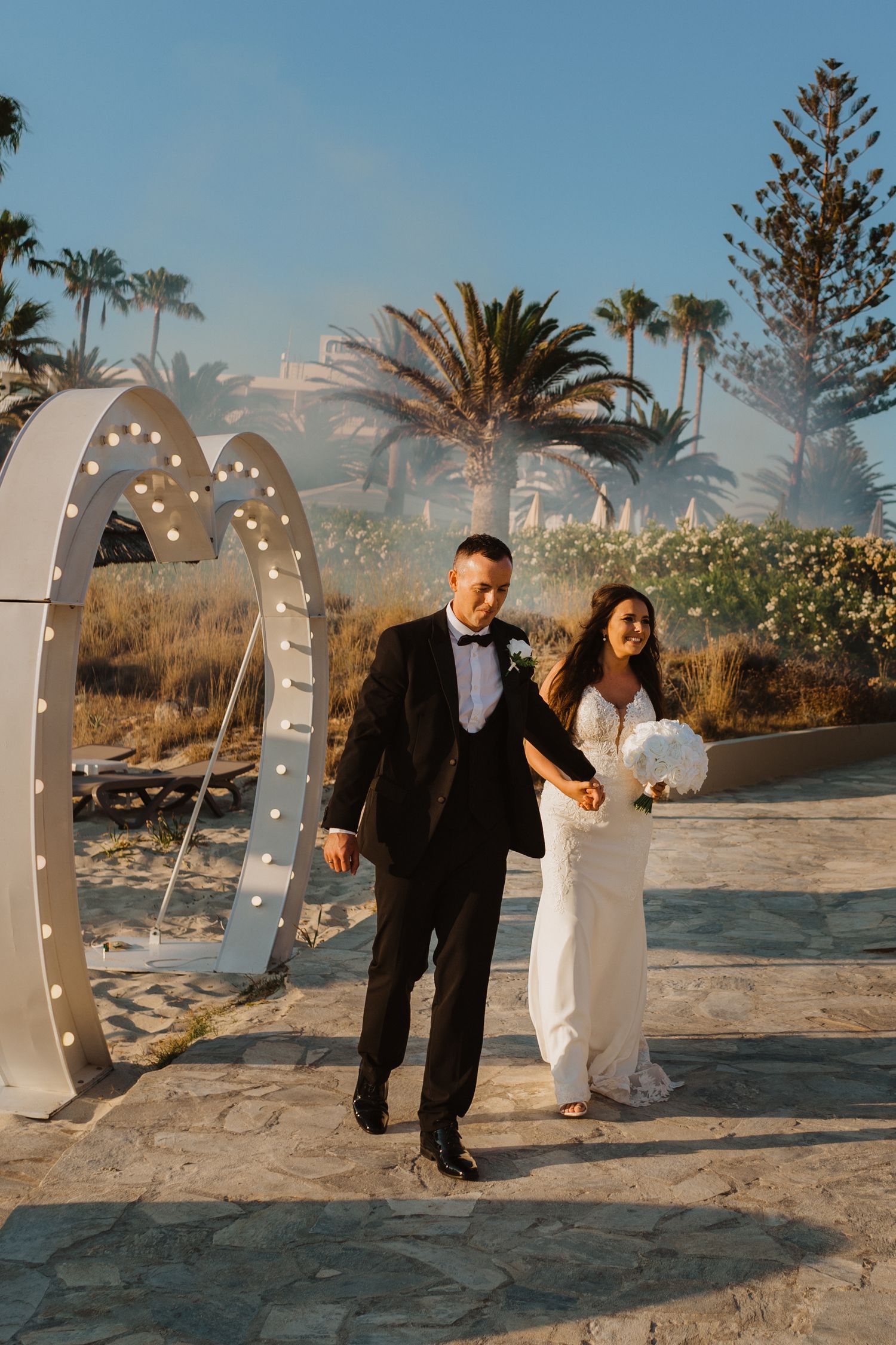 Wedding celebration under decorative arches with string lights at a beachside venue.