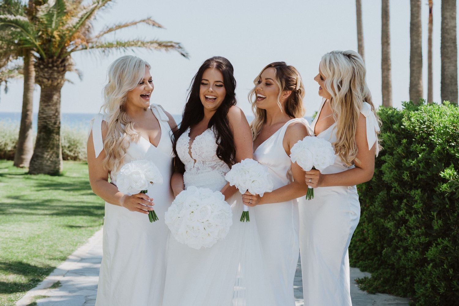 Wedding party laughs together during outdoor photo session by the beach.