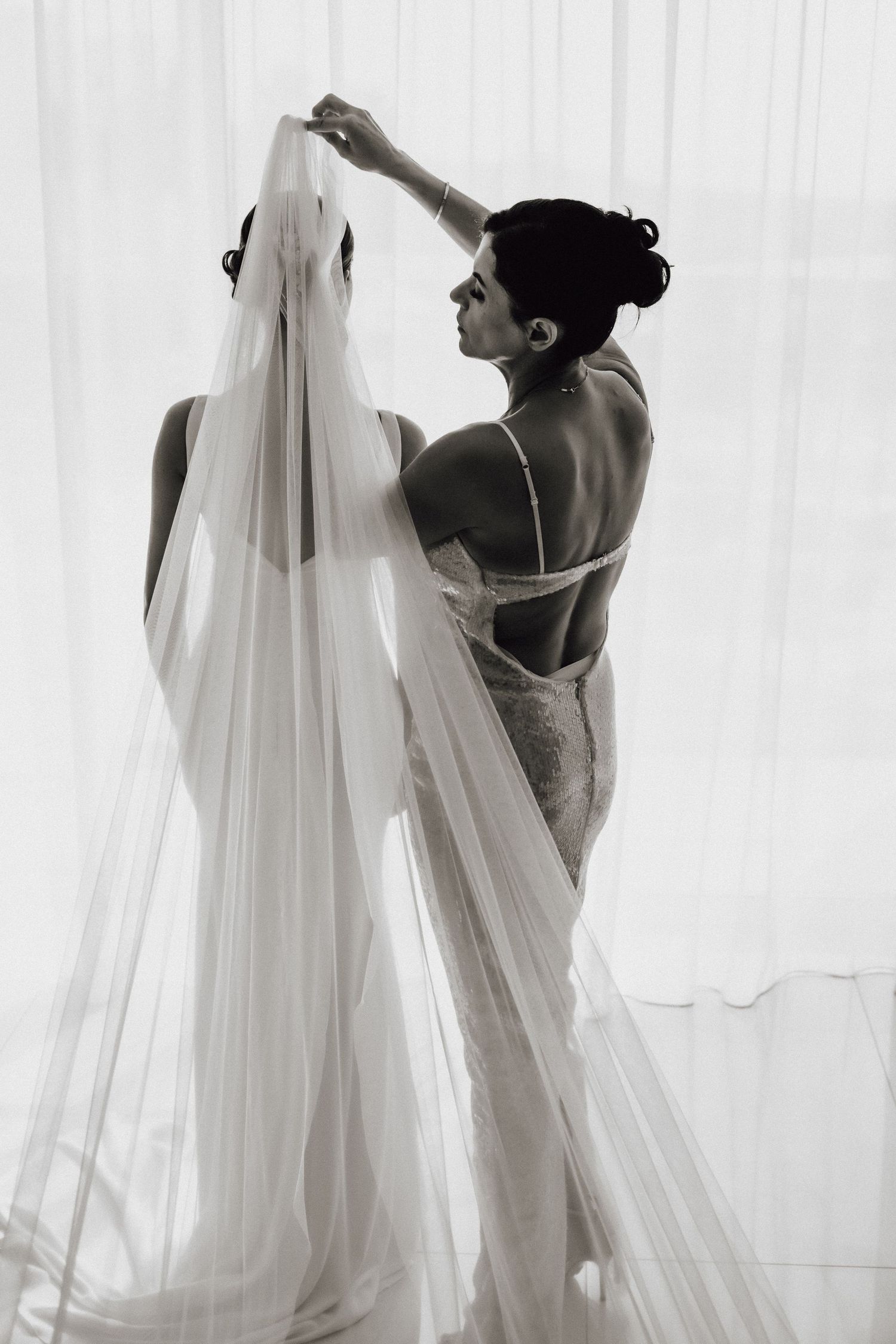 Black and white photo showing final adjustments of a wedding veil in dramatic lighting.