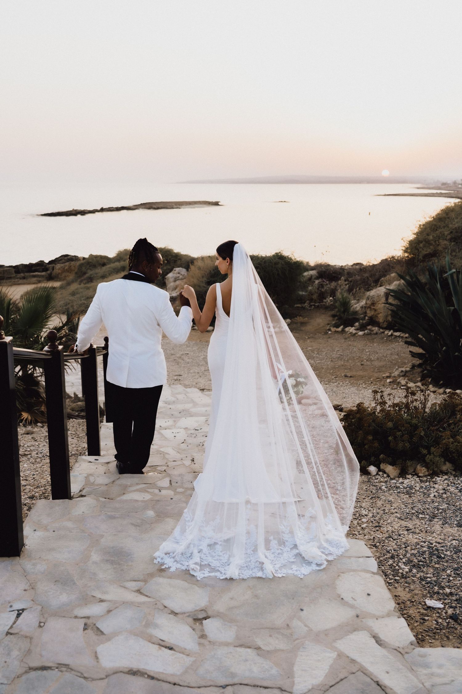 Sunset wedding portrait on stone pathway overlooking Mediterranean coastline.