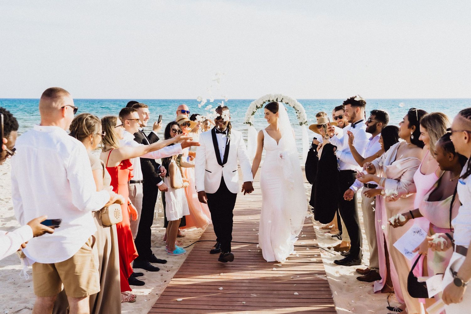Wedding party walking down boardwalk aisle with ocean backdrop.