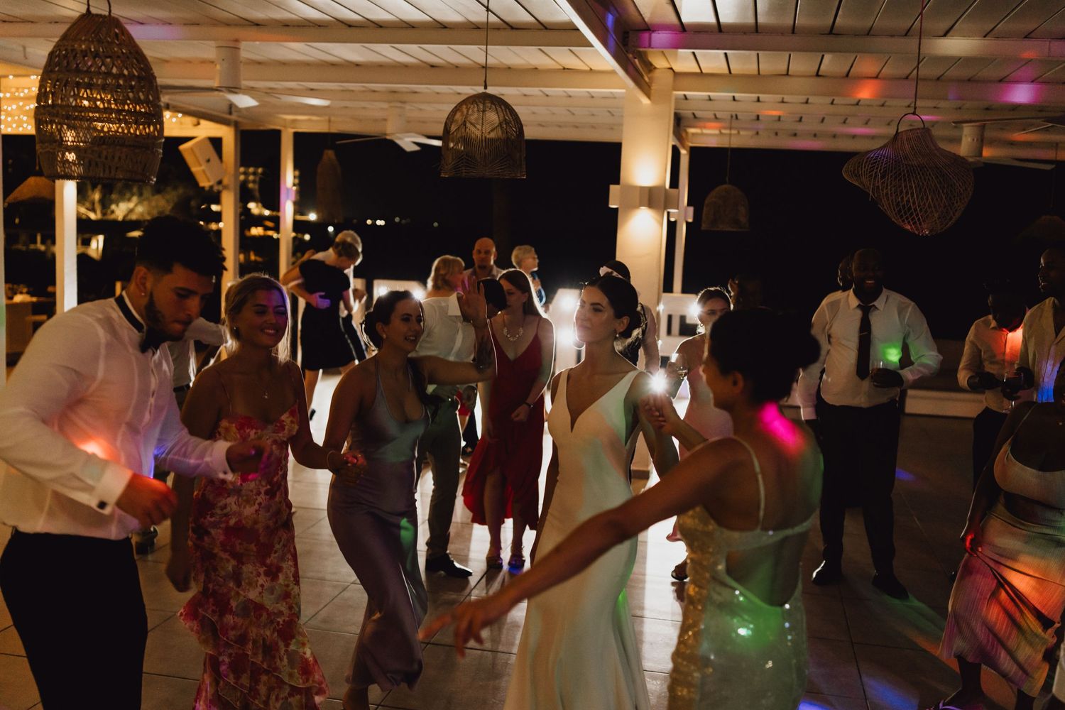 Wedding guests dancing and celebrating on the dance floor under dim lighting and hanging lanterns.