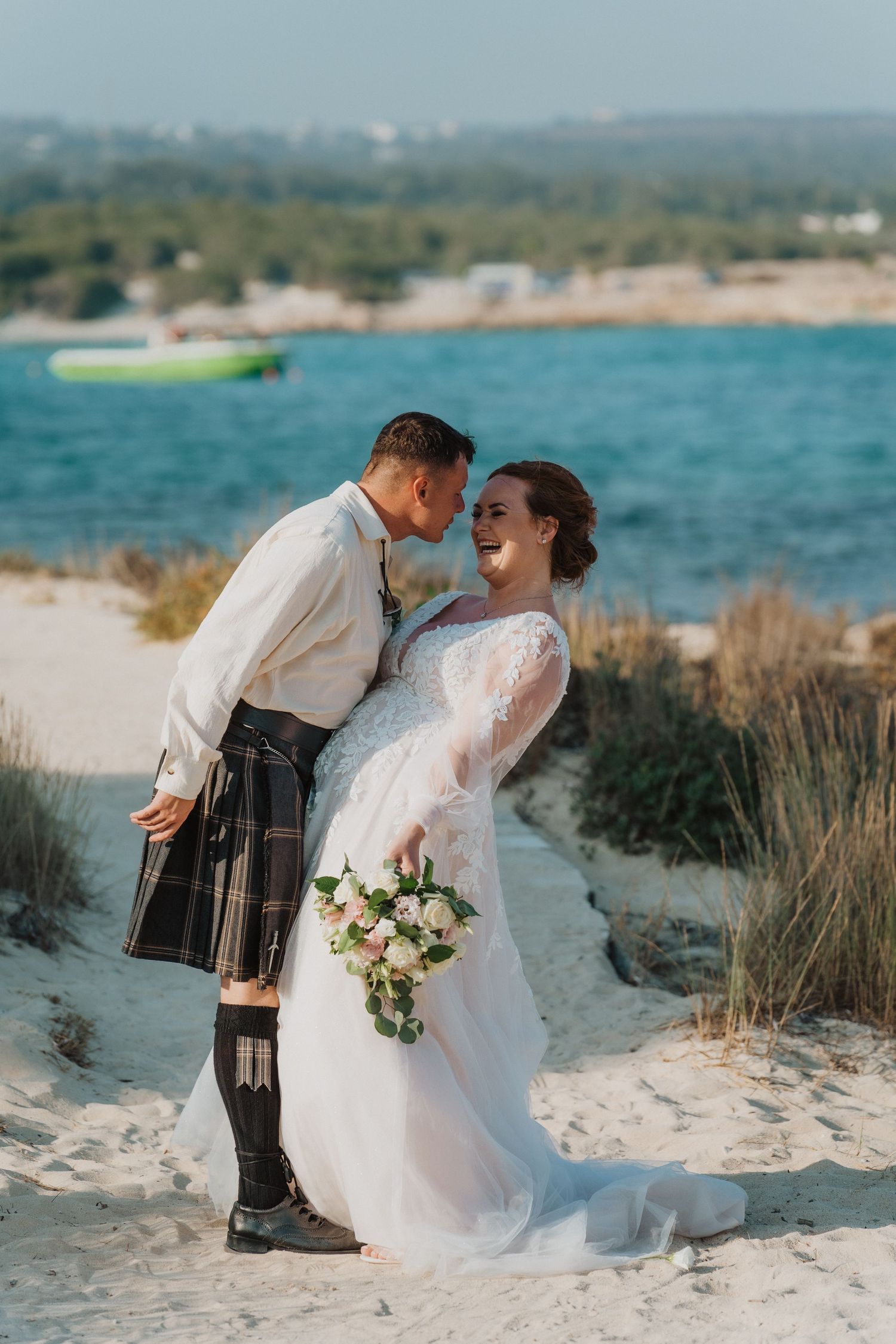 A couple laughs together during their beach wedding photoshoot with scenic coastal views.