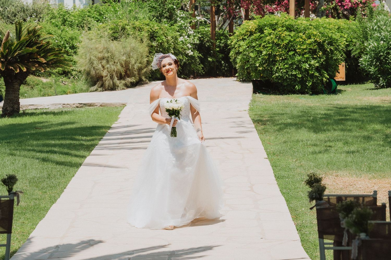 A bride walks down an outdoor path surrounded by tropical landscaping on her wedding day.