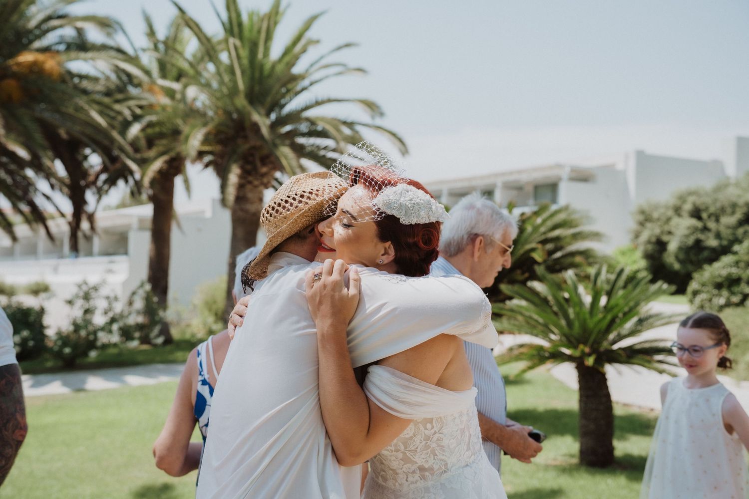 Group embrace during beach wedding with palm trees and ocean backdrop.