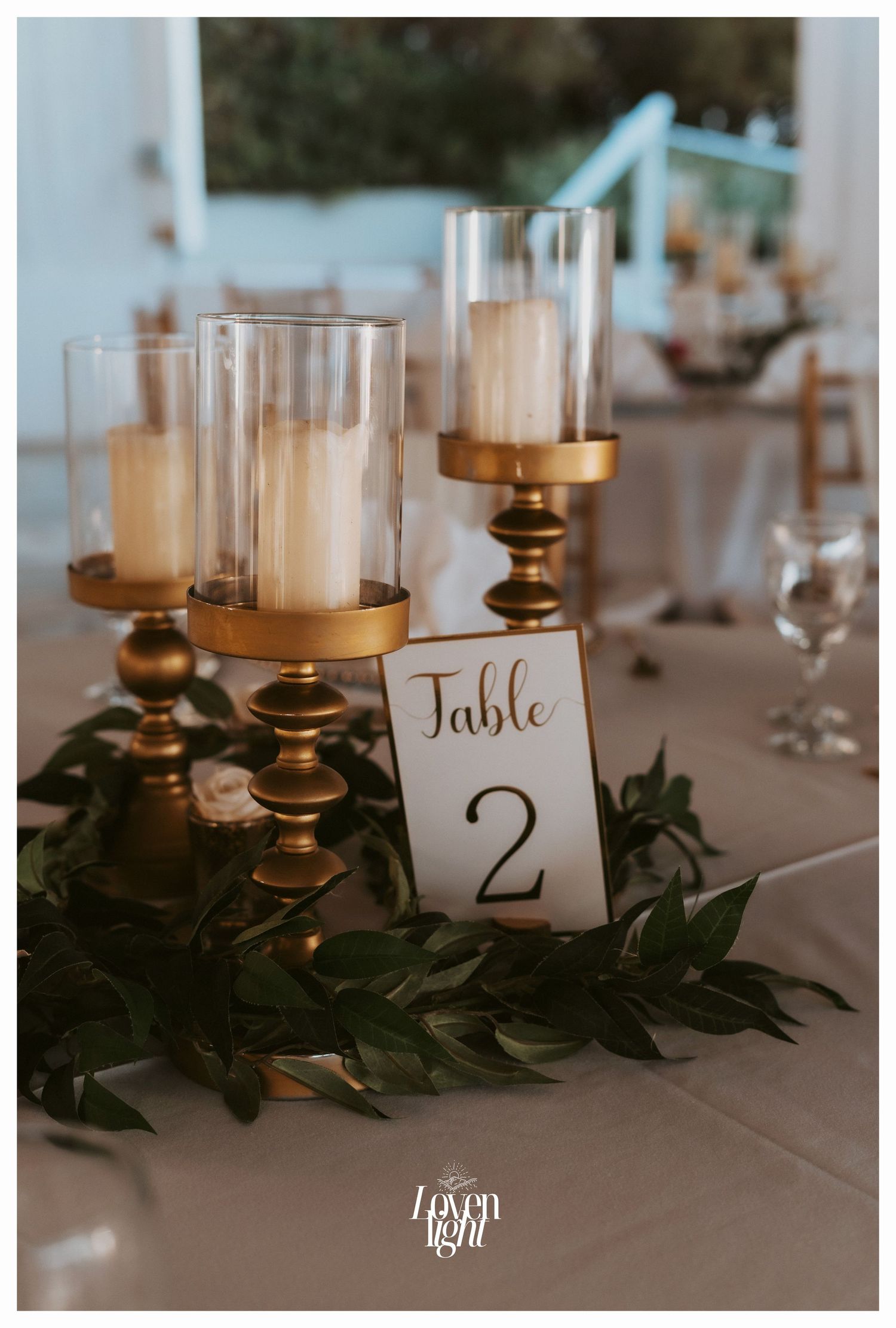 Elegant table decor with gold candlesticks, greenery and Table 2 card marker.