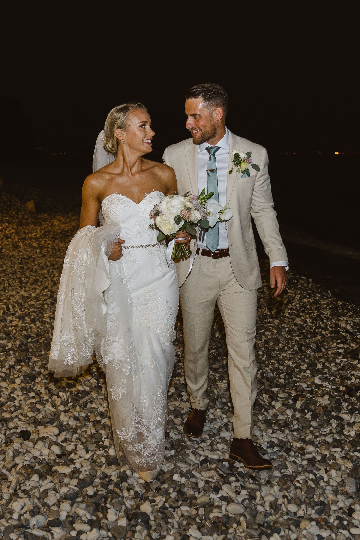 A romantic wedding moment captured on a rocky beach at night.