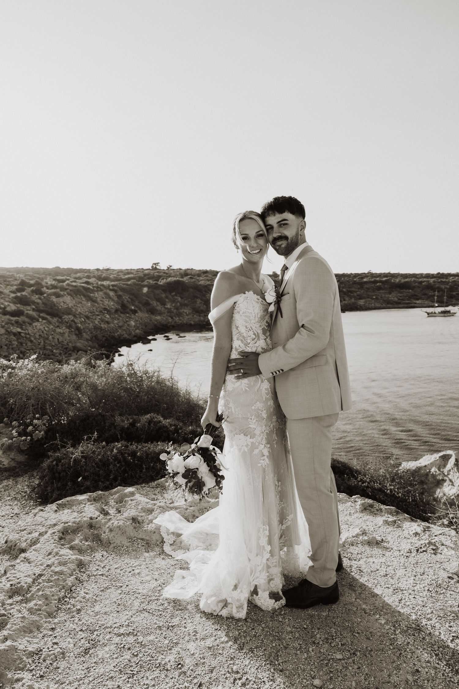 Black and white wedding portrait on coastal overlook with serene water views.