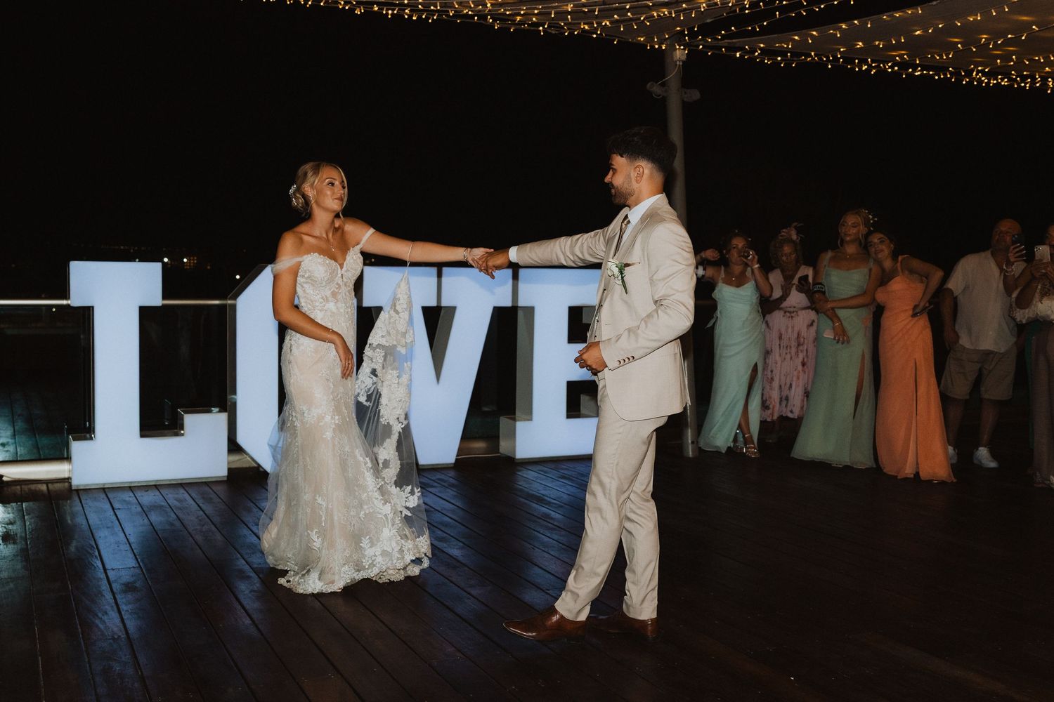 Couple dancing by illuminated LOVE letters at outdoor evening wedding reception.