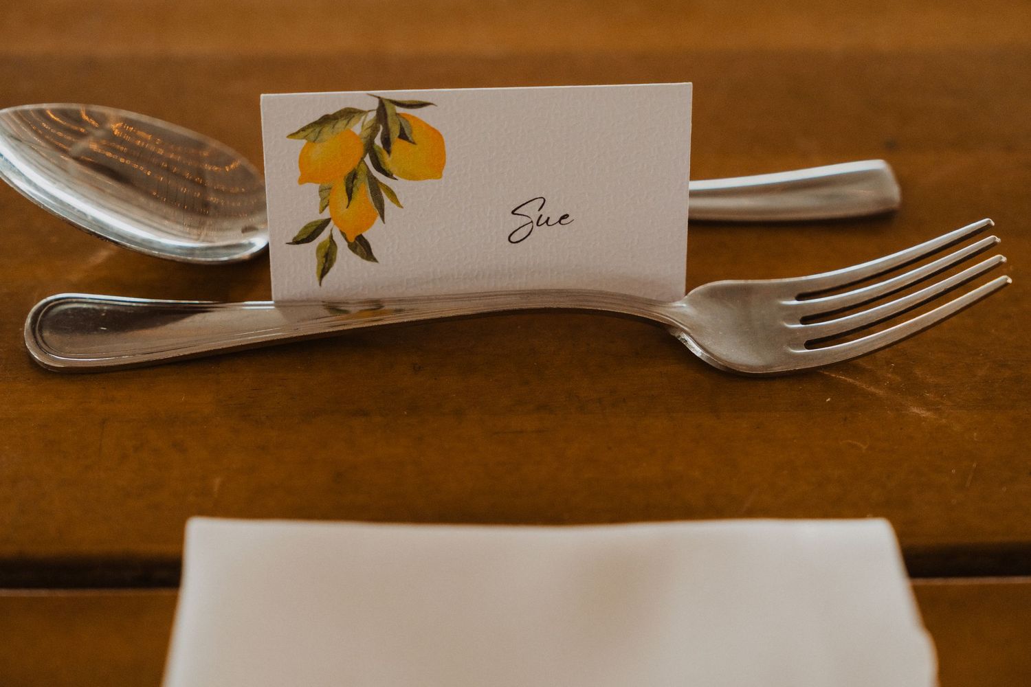 Wedding table place setting with lemon-themed name card and elegant silverware on wooden surface.