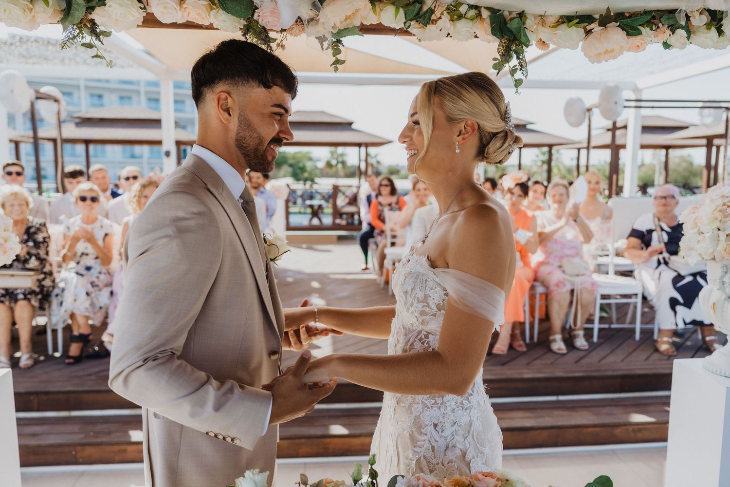 Romantic moments unfold during a beach wedding ceremony under floral garlands.