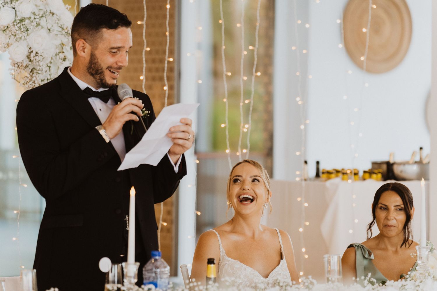 Wedding guests raise champagne glasses during a joyful toast at an elegant reception with twinkling lights in background.