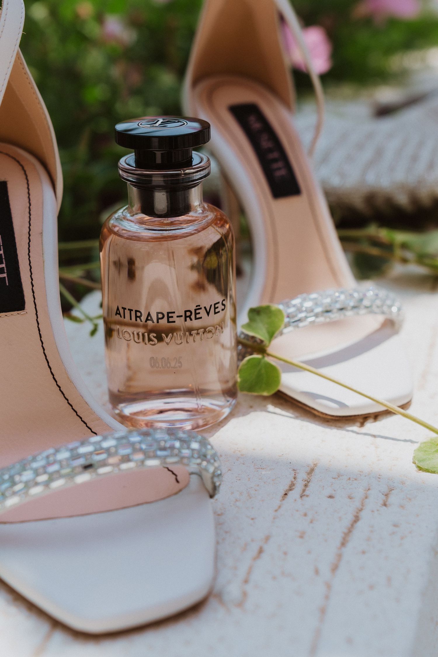 Louis Vuitton Attrape-Rêves perfume bottle displayed with elegant white heeled sandals on a white surface.