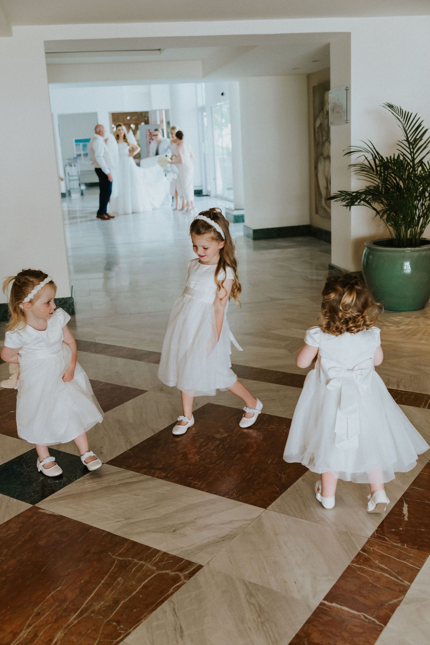 Young attendants in white dresses playing on a modern checkered floor during wedding preparations.