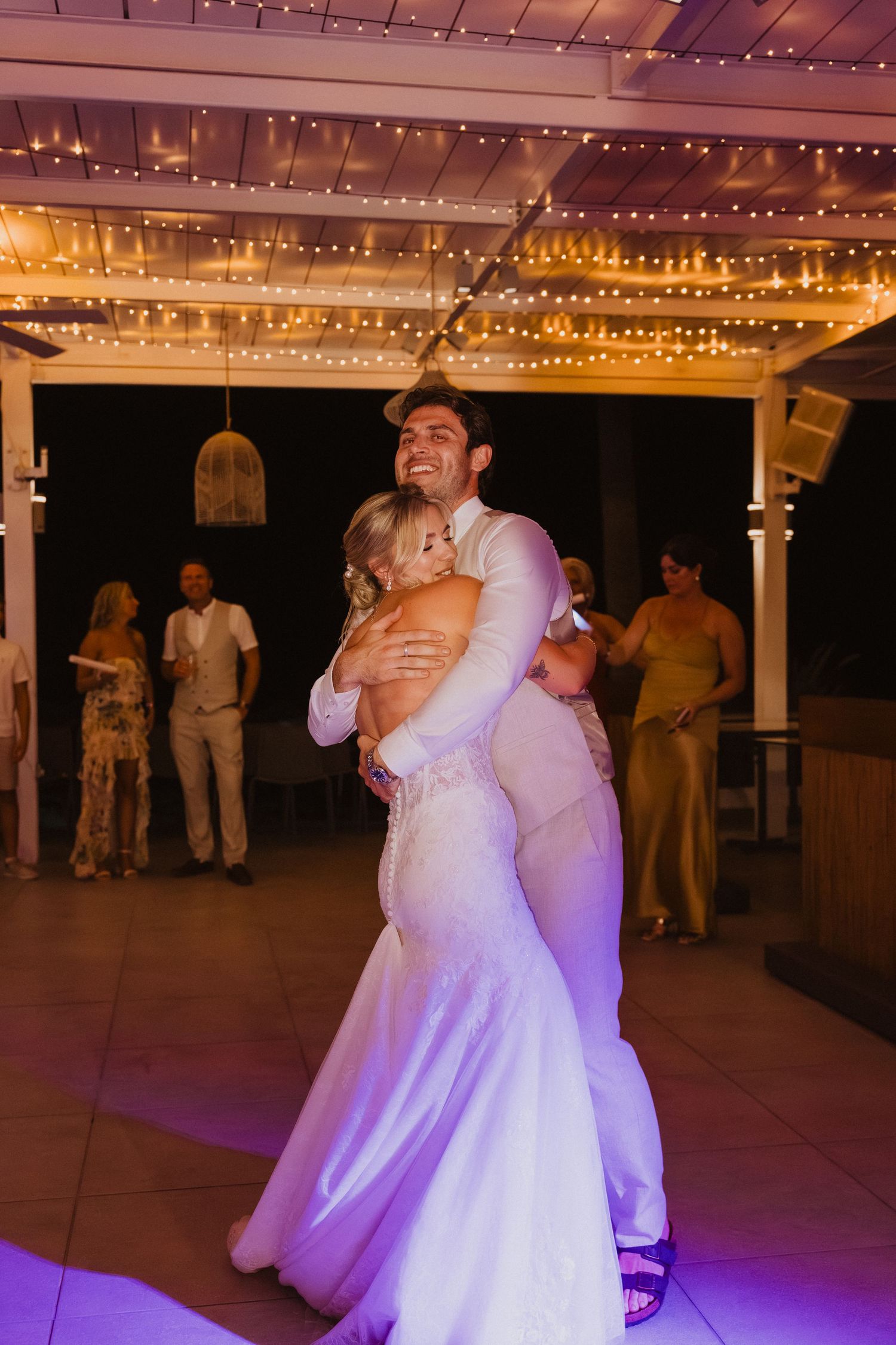 Couples dancing under twinkling string lights at an evening wedding reception.