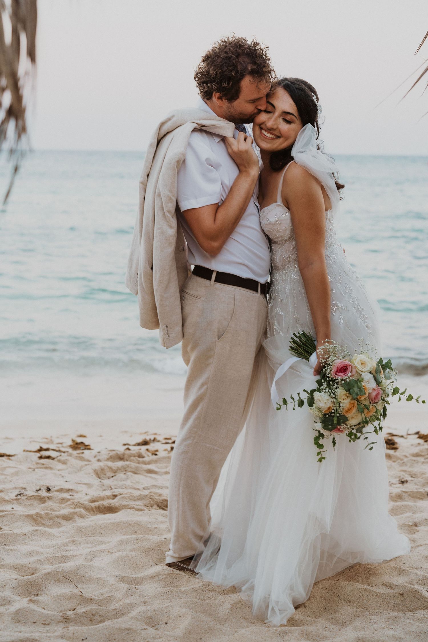 Intimate beach wedding portrait with palm trees and ocean in background.
