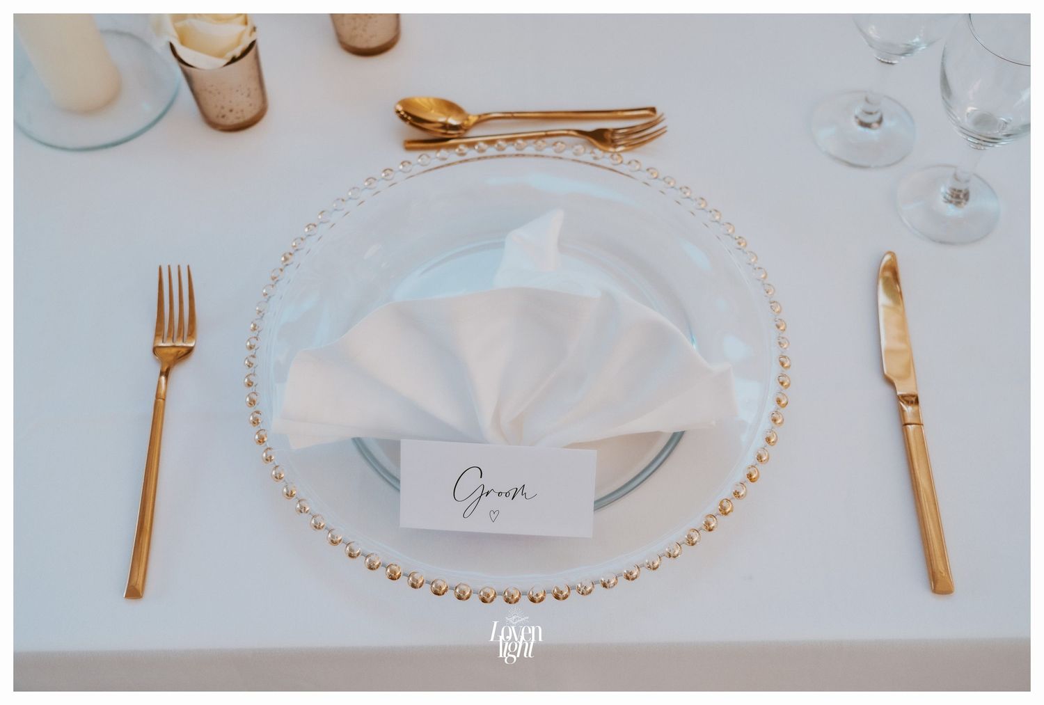 Elegant place setting with gold cutlery and beaded glass charger plate featuring a white folded napkin.