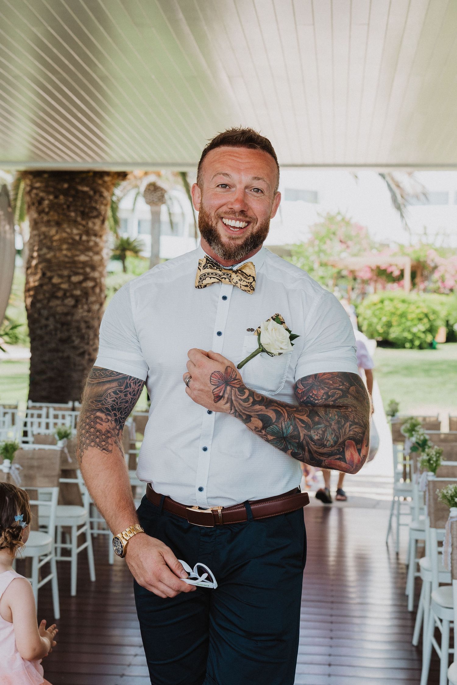 Wedding attendant in white shirt and bow tie standing at outdoor venue.