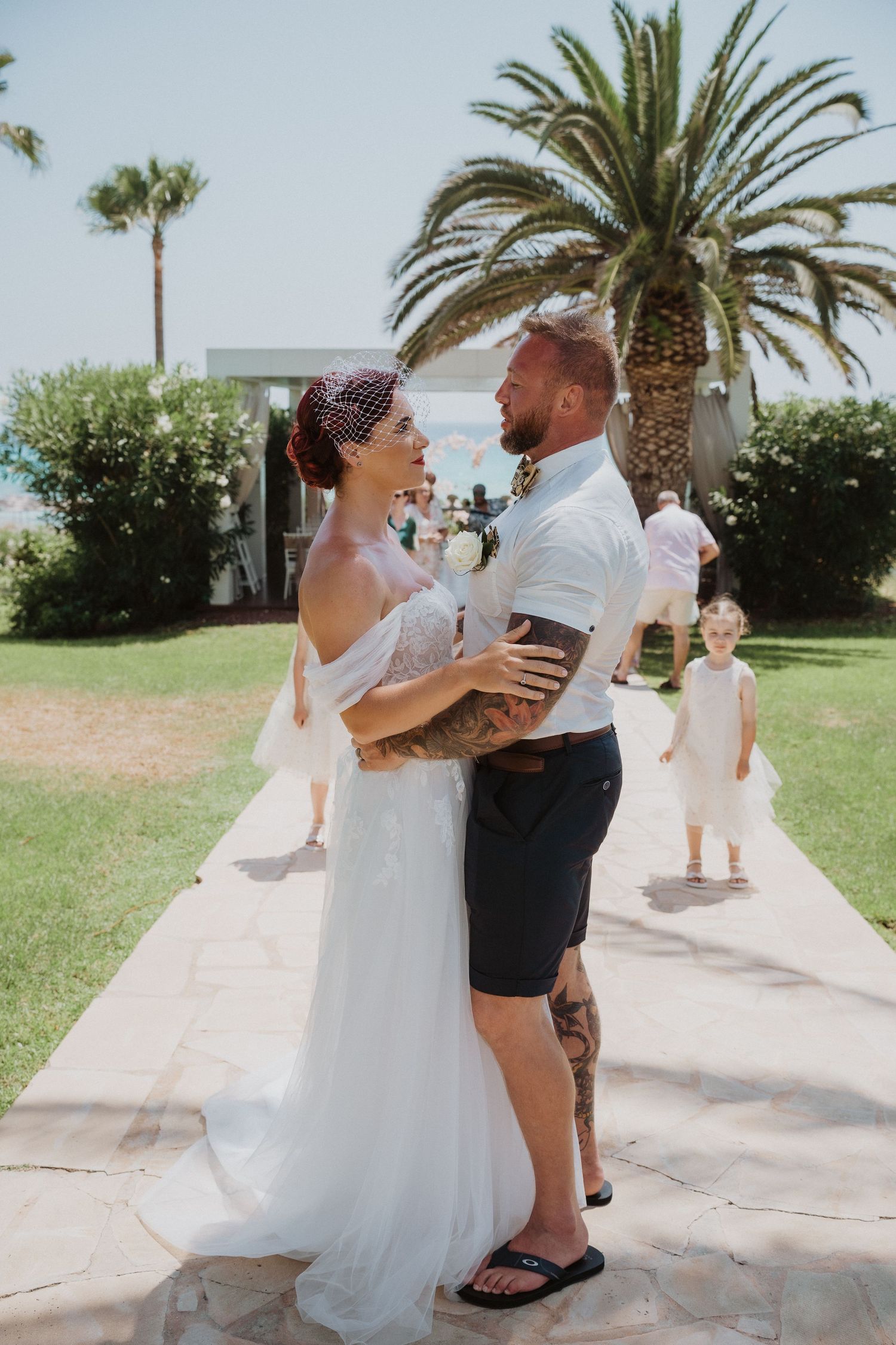 Wedding couple embraces outdoors under palm trees at a tropical destination venue.