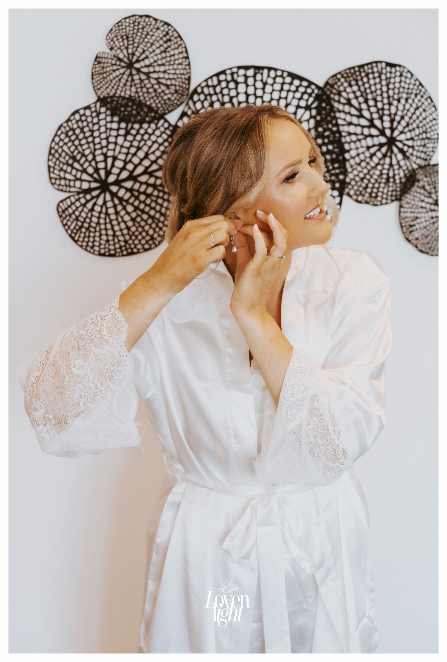 Someone wearing a white robe putting on earrings against a wall with circular decorative elements.