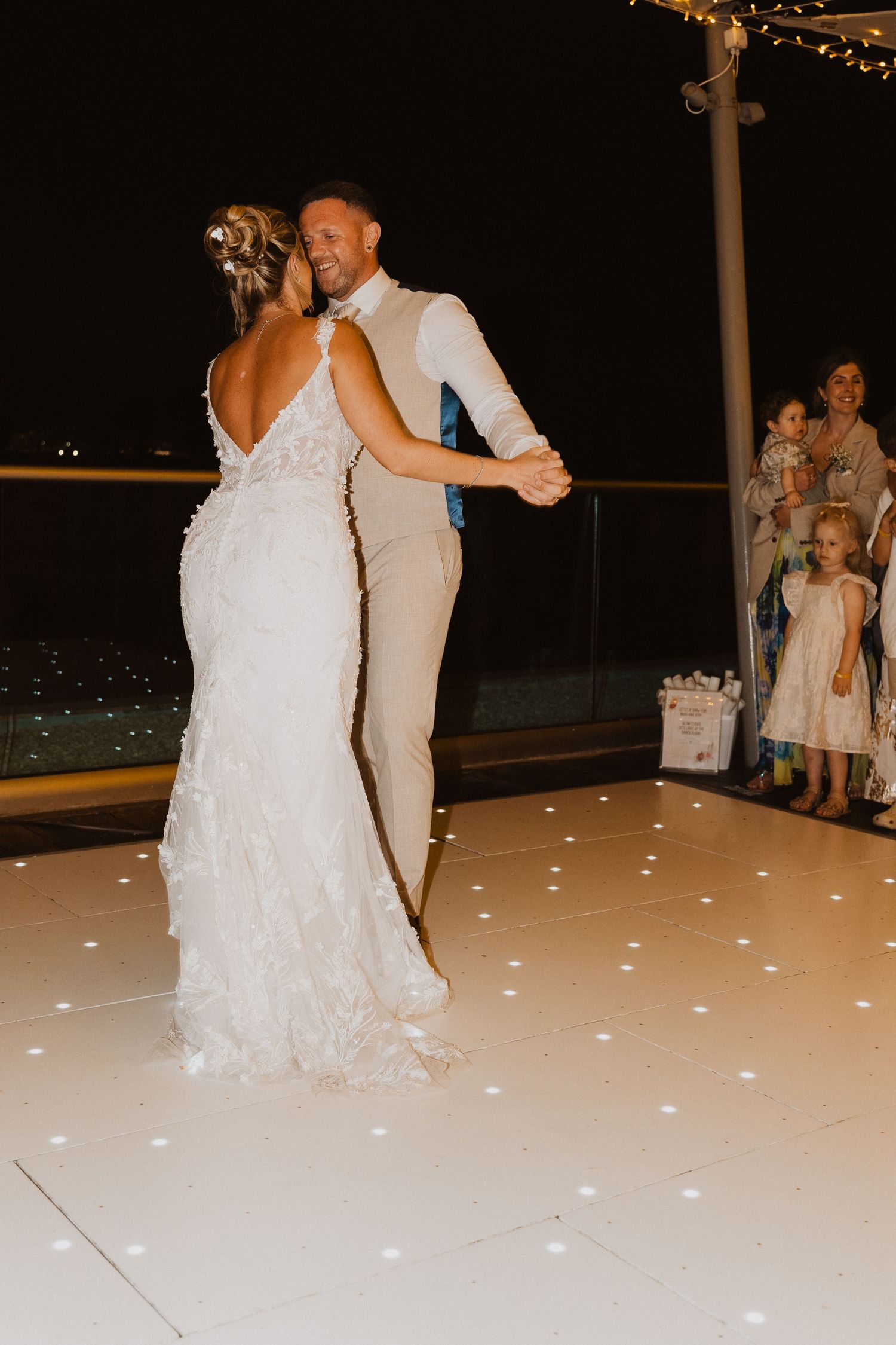 A couple shares their first dance on an illuminated white dance floor at an elegant evening wedding reception.