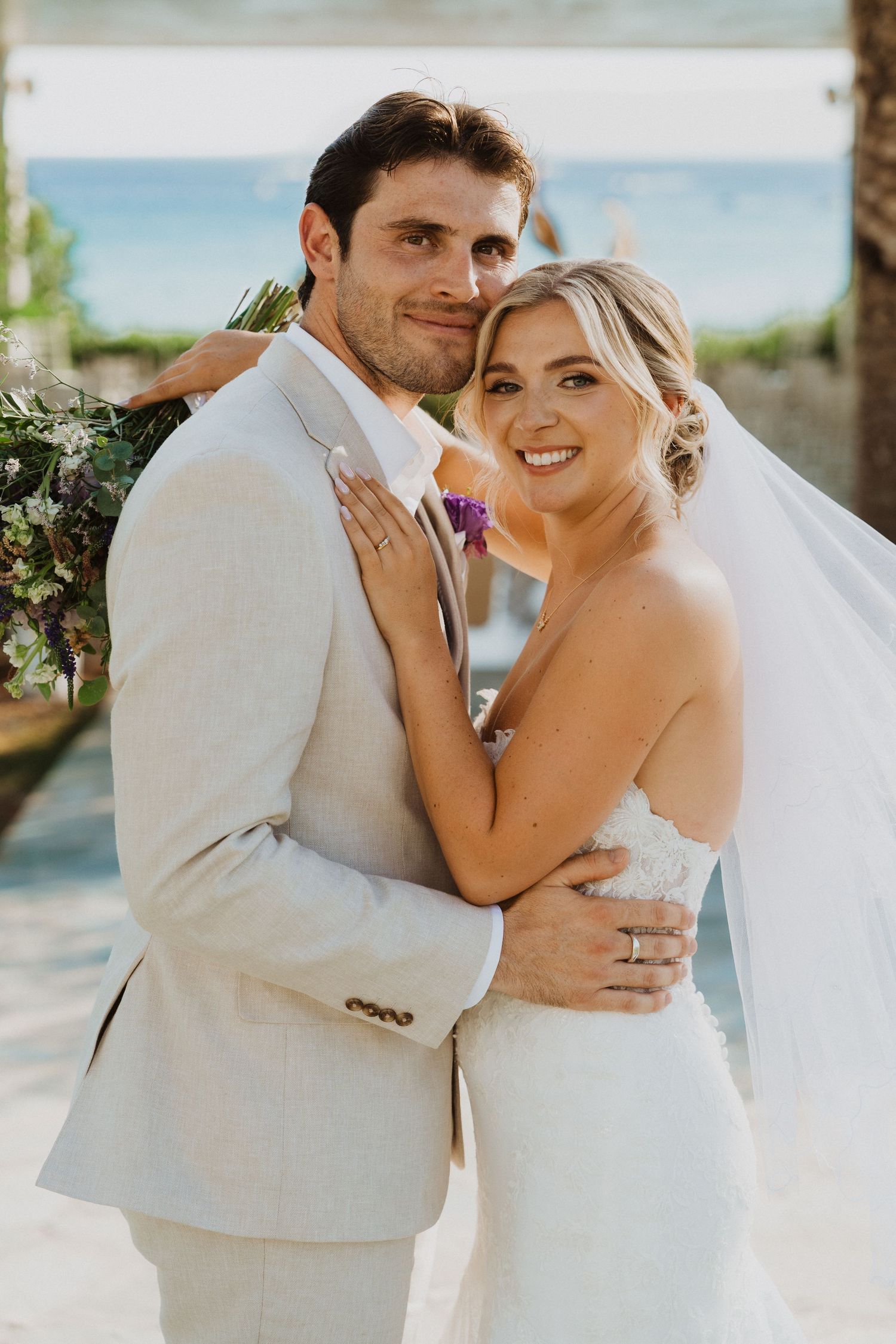 A romantic wedding portrait captured outdoors with an ocean backdrop and tropical scenery.