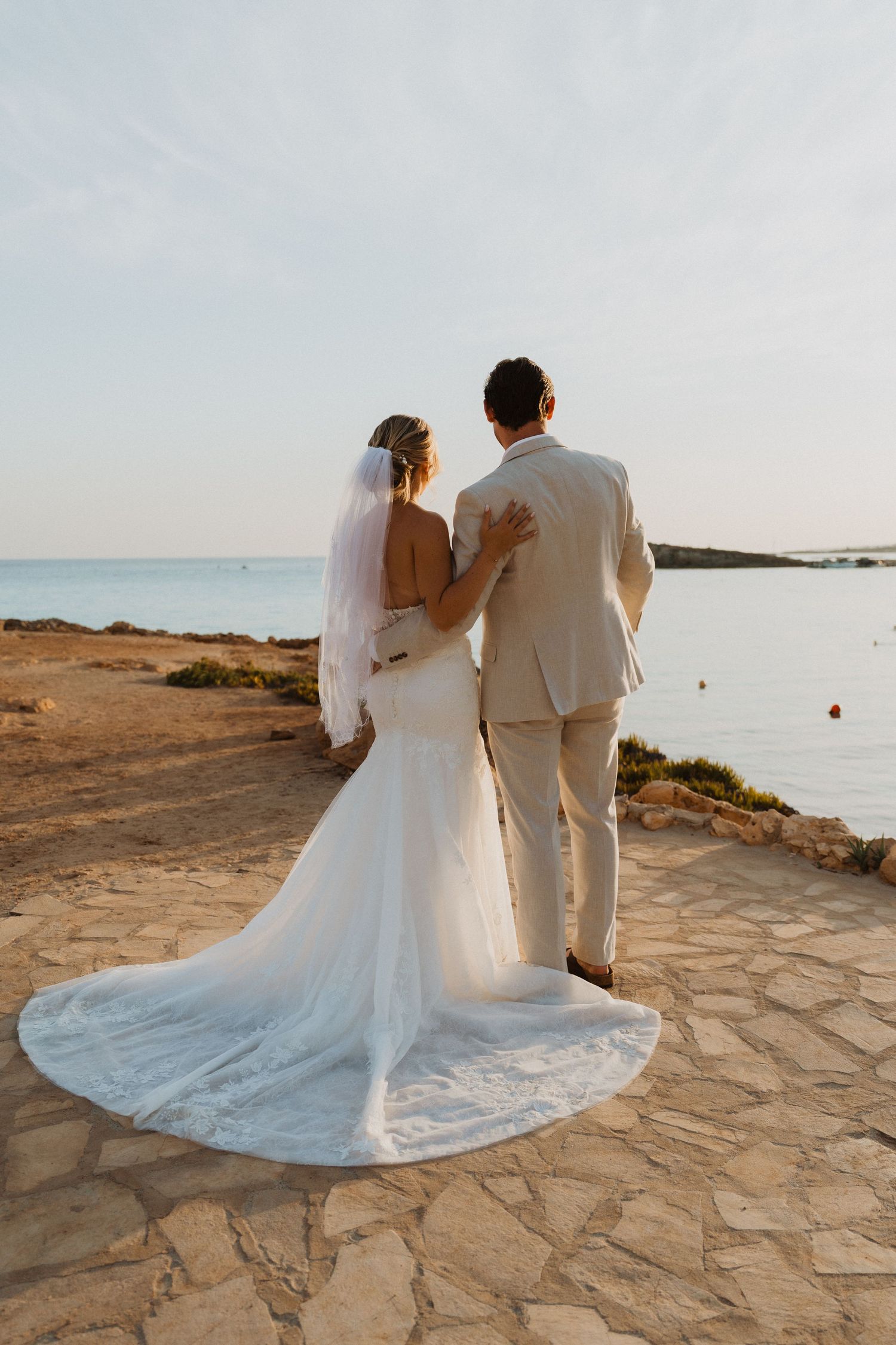 Dramatic silhouette of wedding couple embracing on coastal rocks during sunset.