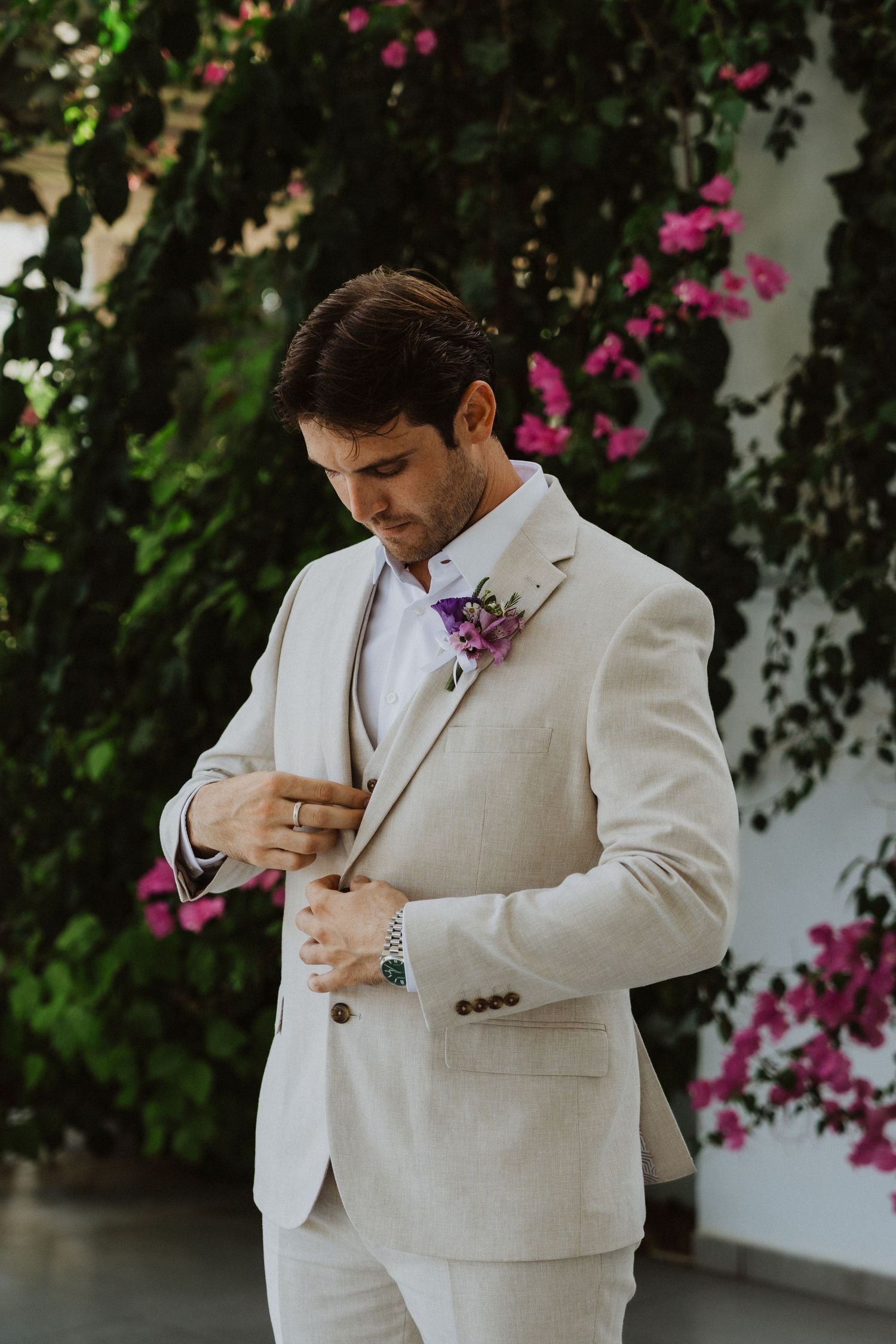 Multiple shots of groom adjusting his tie before ceremony with pink bougainvillea in background.