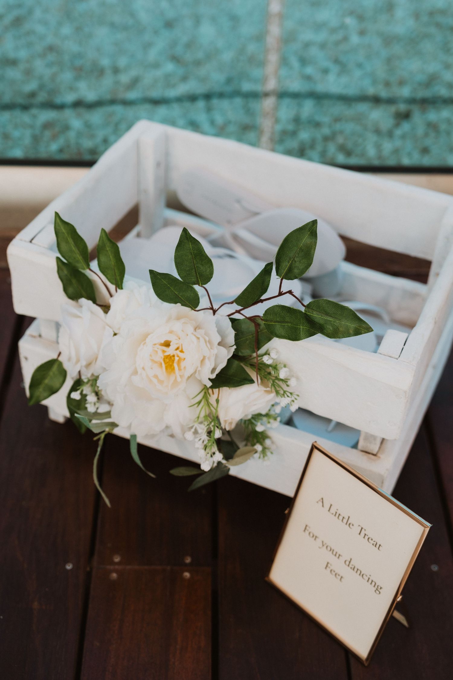 White wooden crate with white peony floral arrangement and a small sign reading A Little Treat For Your Dancing Feet.