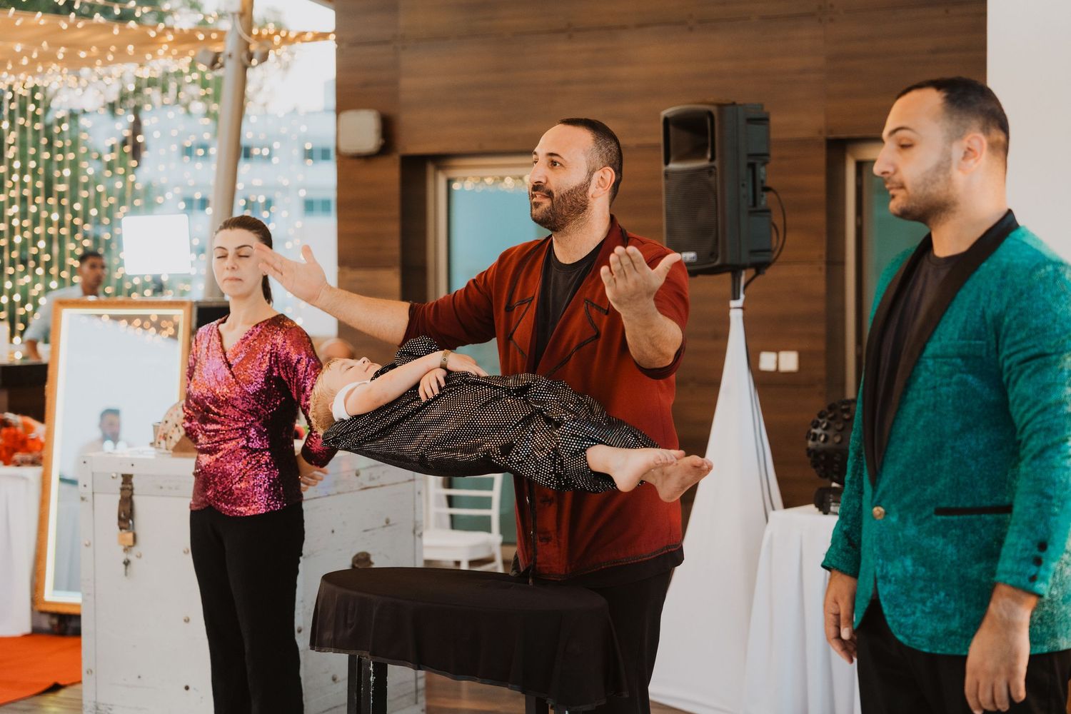 Magician levitating a person during a live stage performance with two assistants in colorful attire.