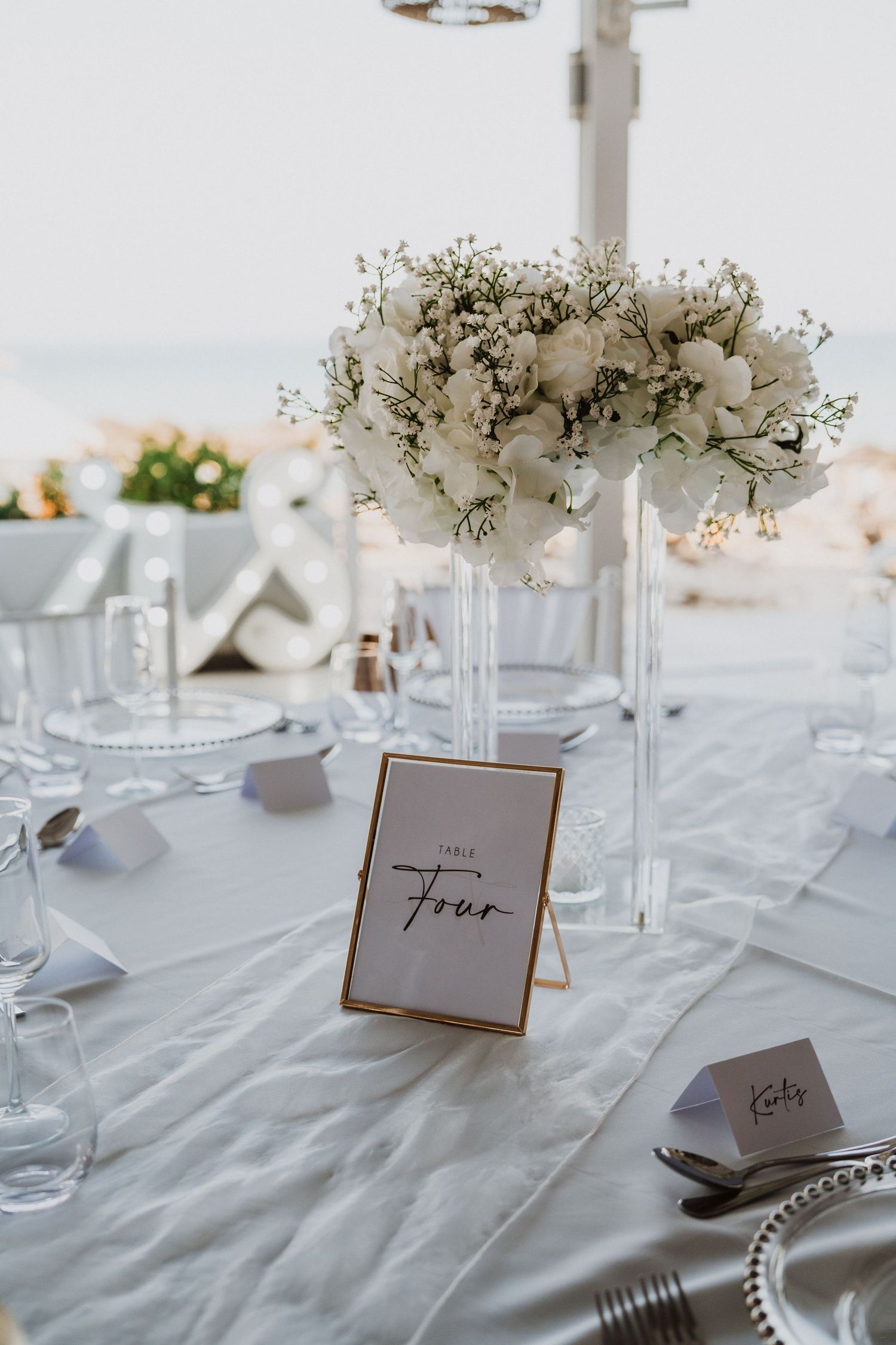 Elegant white wedding reception table settings with baby's breath centerpieces and table numbers.