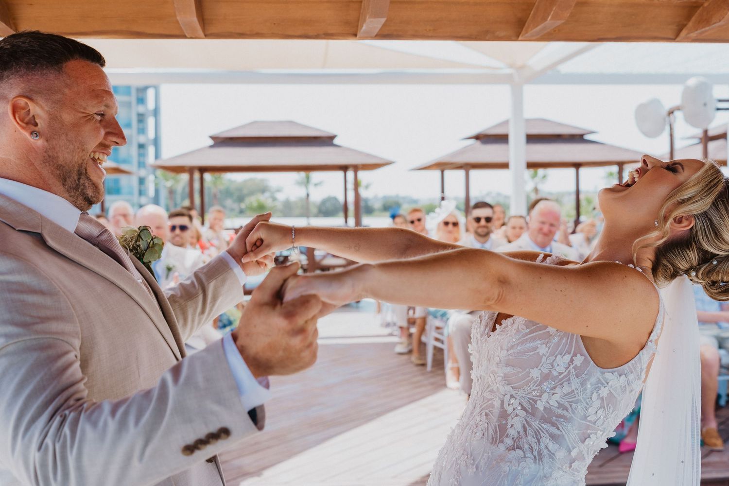 Wedding guests enjoy a festive celebration at an outdoor reception venue with wooden beams and white decor.