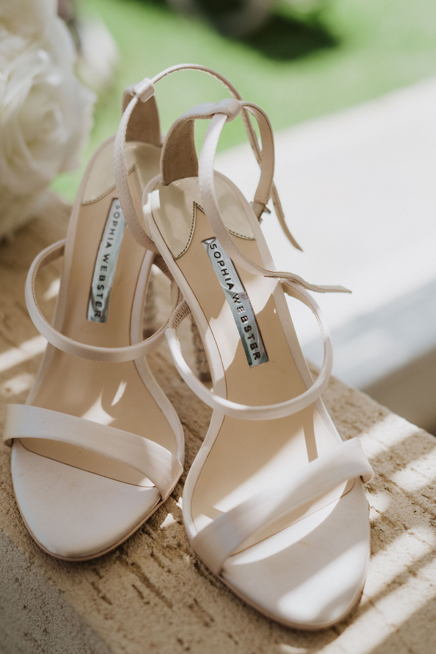 Elegant white strappy wedding sandals with delicate design details photographed in natural light.