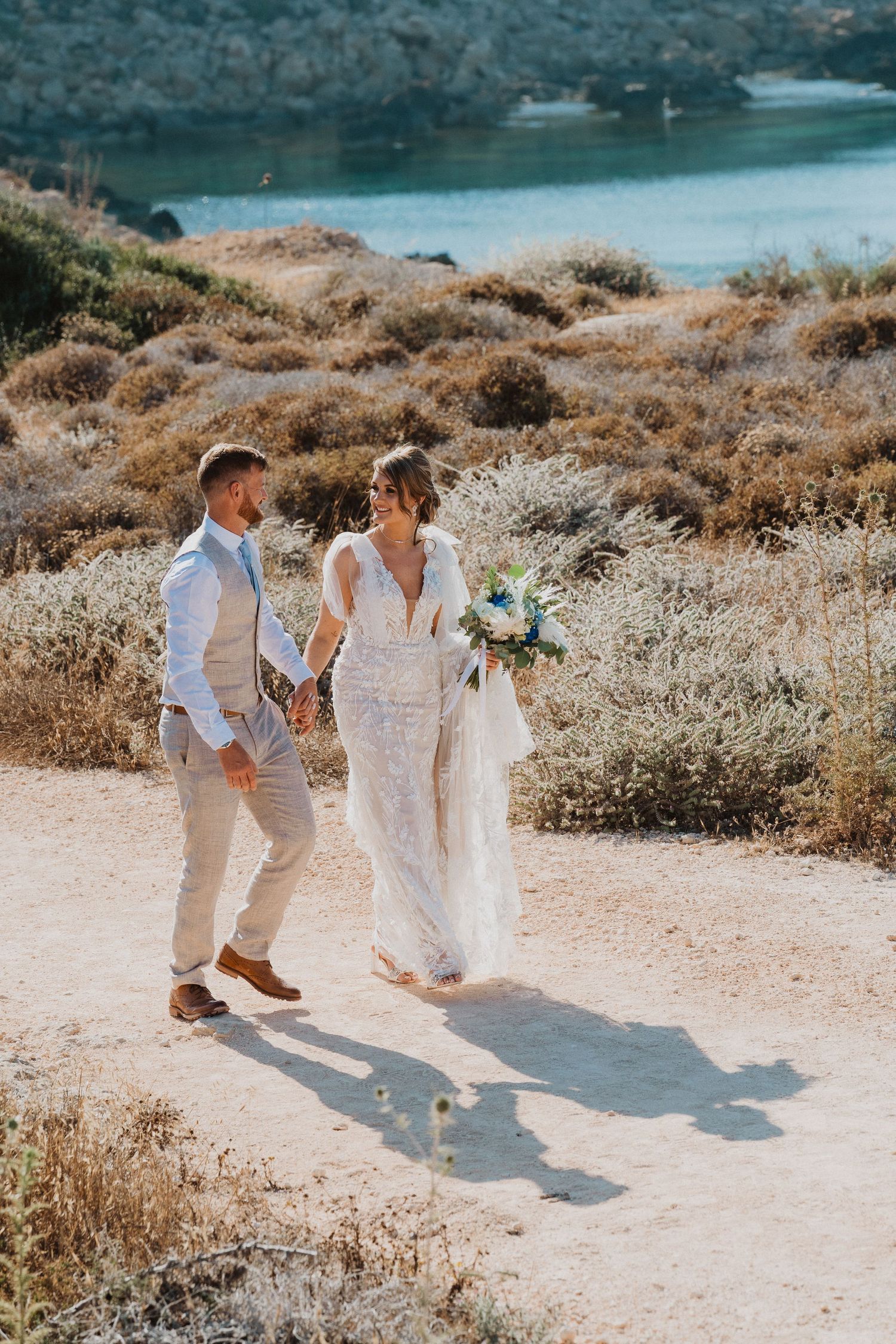 Wedding couple walking hand in hand along a scenic coastal trail.