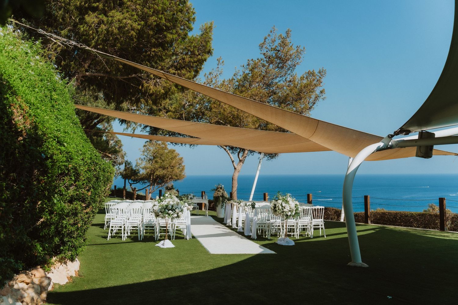 Elegant outdoor wedding reception setup with white tables under sail shades overlooking a blue ocean view.