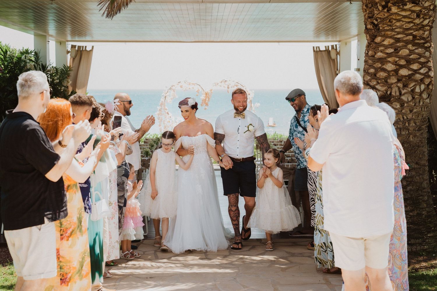 Wedding guests line up to celebrate the newlyweds under a covered walkway.