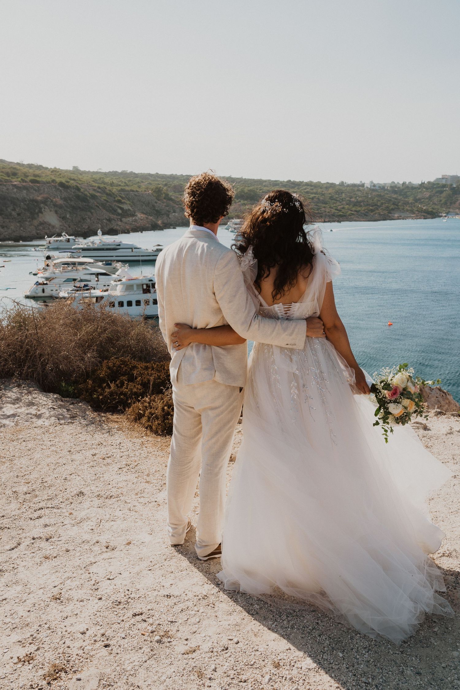 A serene wedding photo showing a couple overlooking a Mediterranean harbor filled with boats.