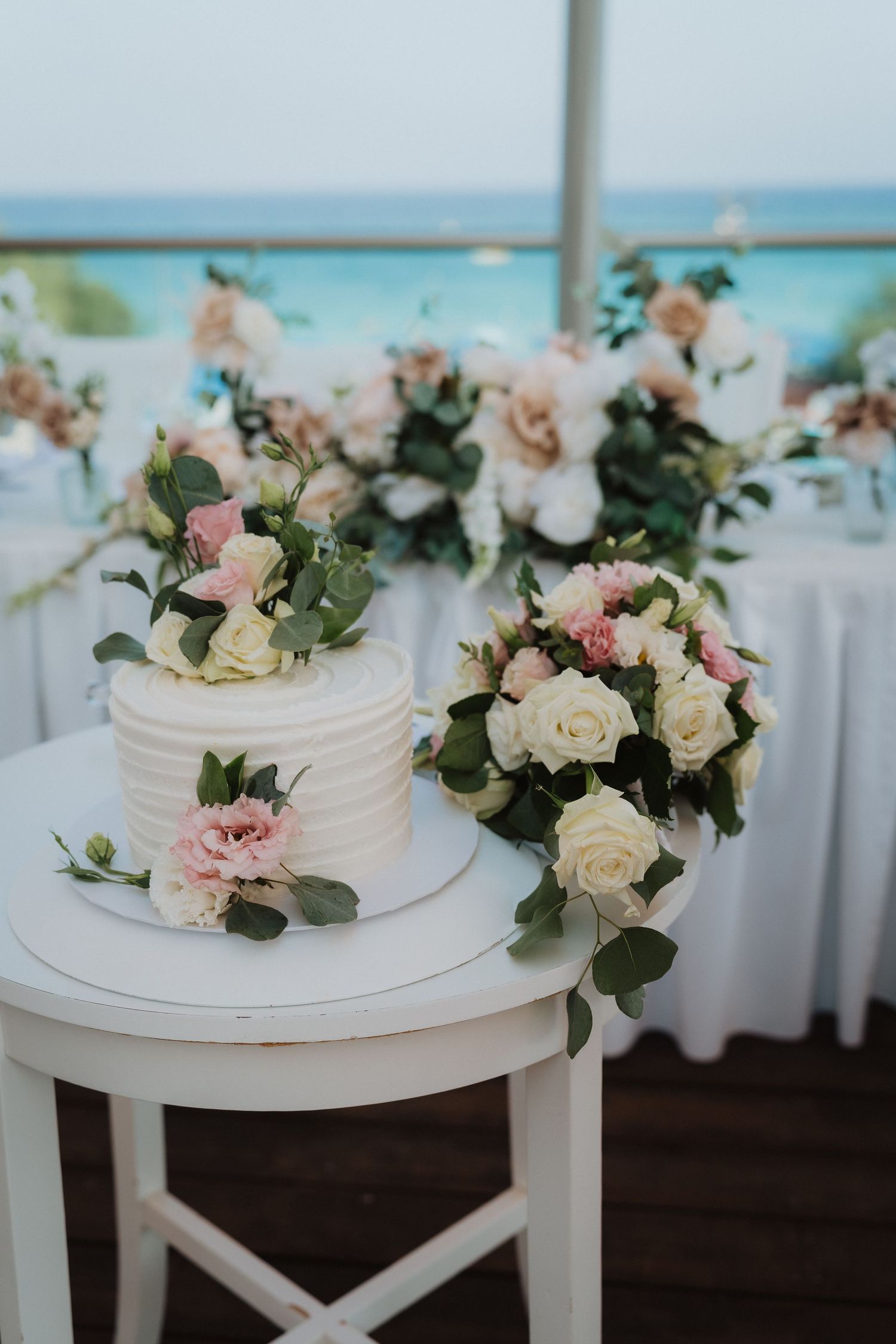 White wedding cake and floral arrangements on display at oceanfront reception venue.
