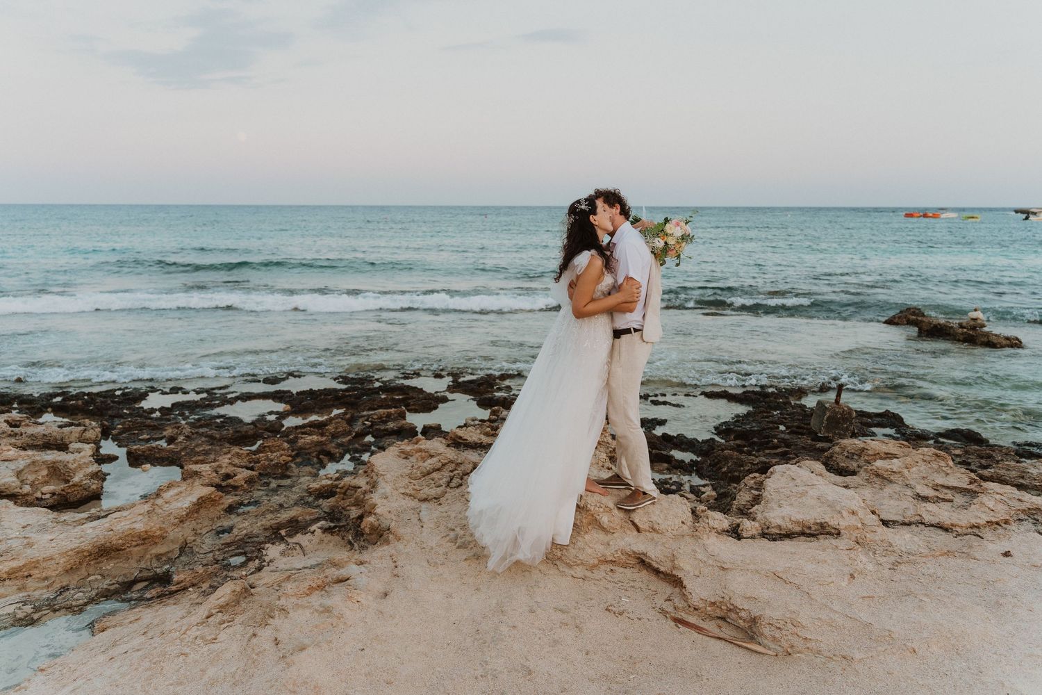 A loving embrace captured on rocky coastline during a beach wedding ceremony.