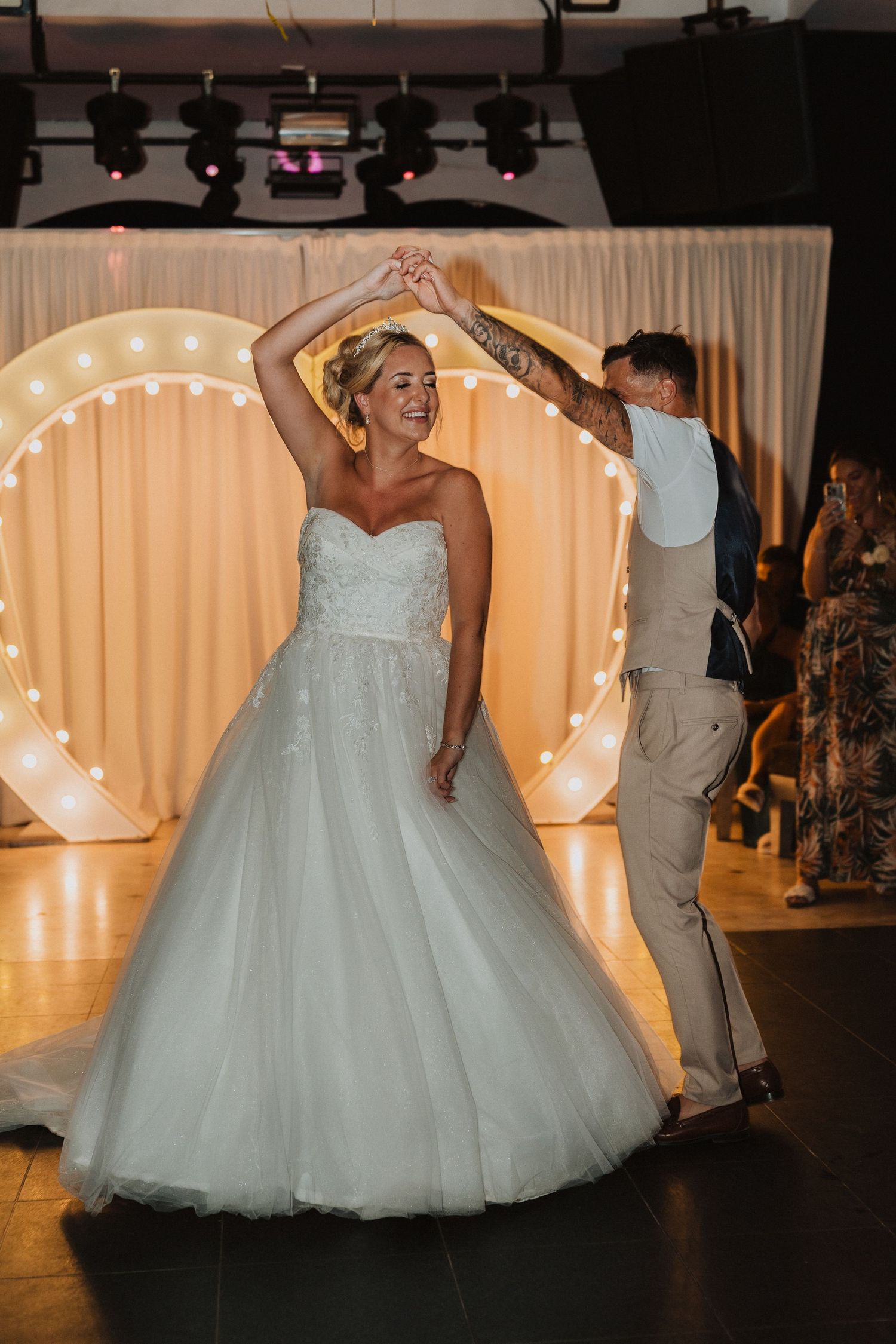 A dancing moment captured under a heart-shaped light display at a wedding reception.