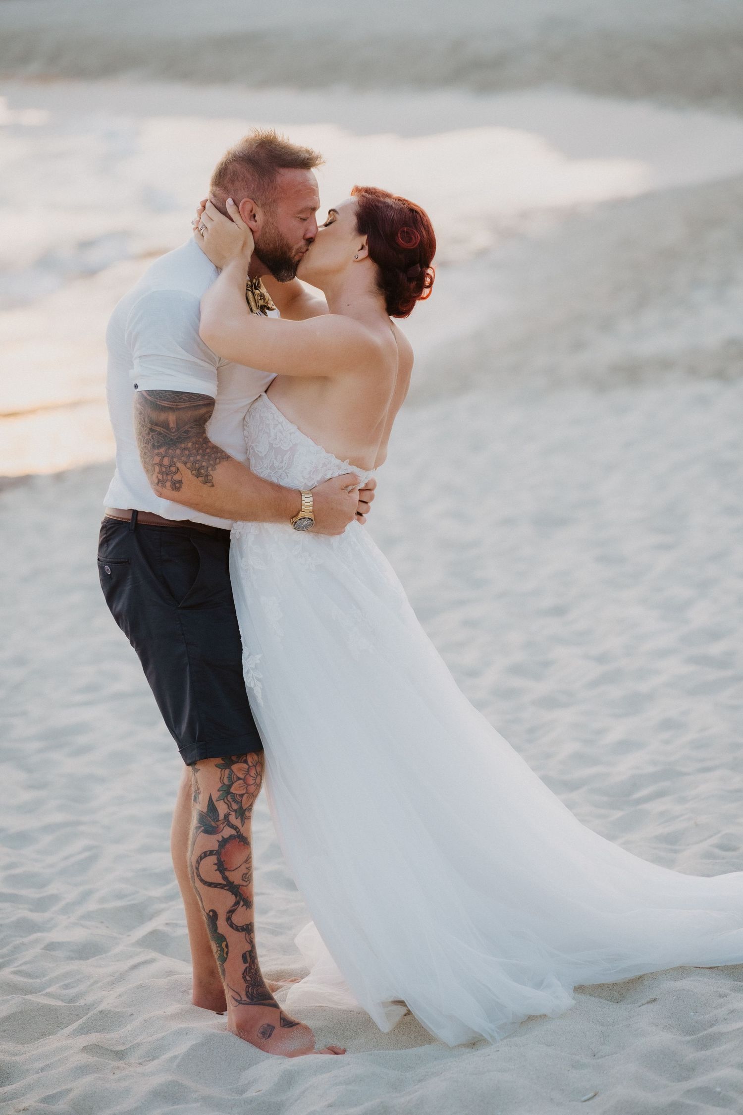 Romantic beach wedding photo at sunset with white wedding dress flowing in breeze.