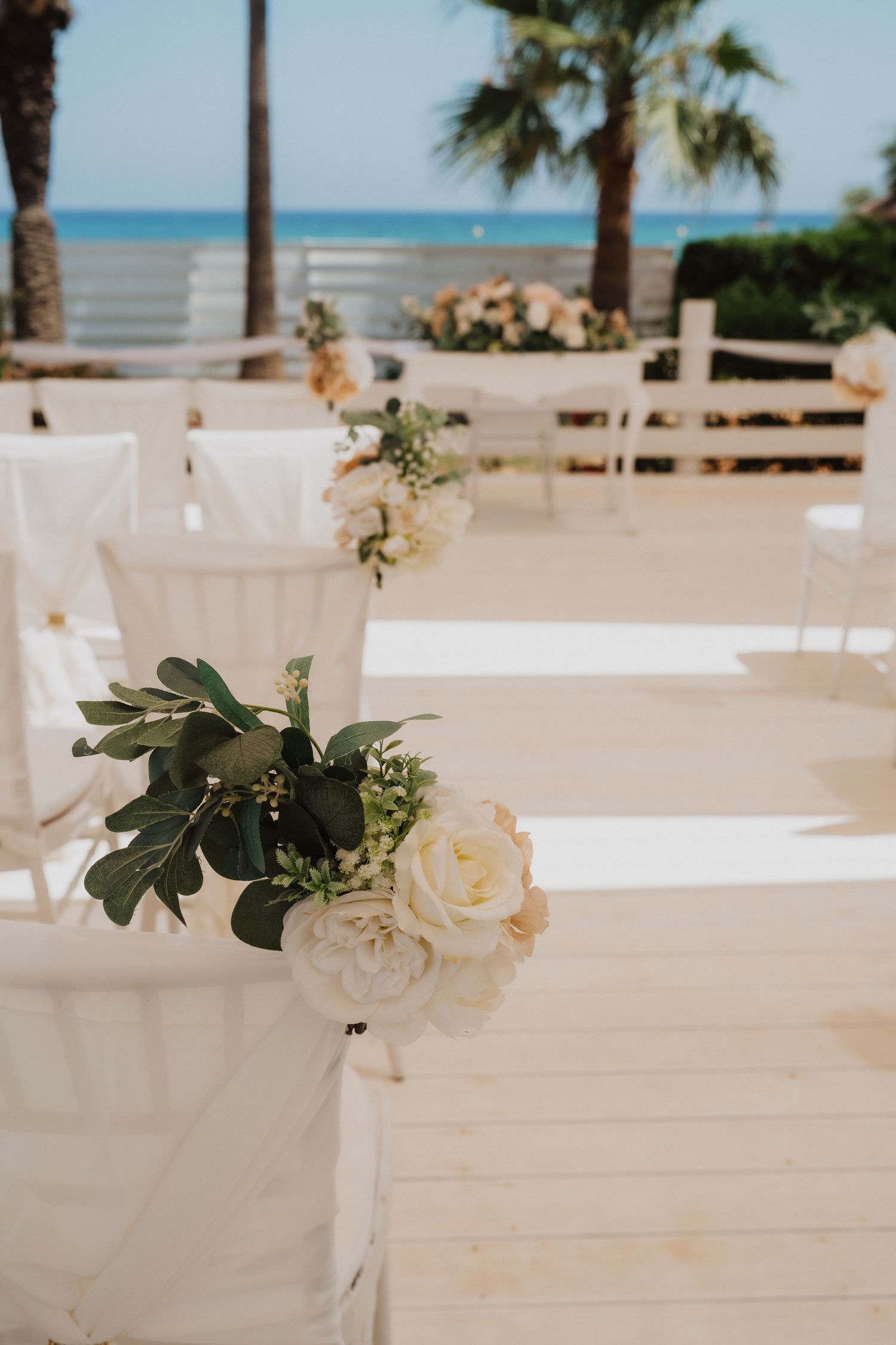 White ceremony chairs with floral decorations set up on a deck overlooking the ocean.