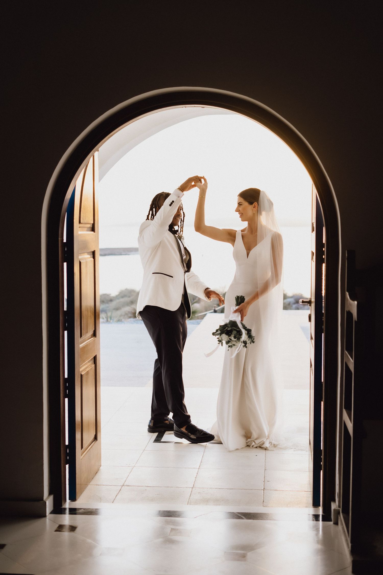 Wedding couple dances and celebrates in an elegant arched doorway.