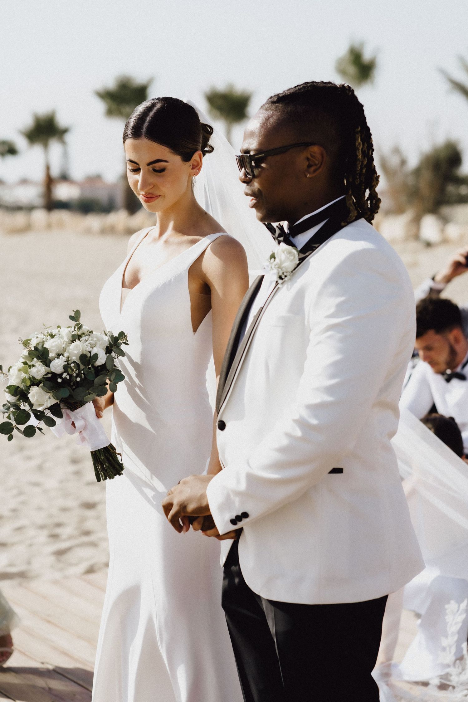 Elegant beach wedding ceremony with couple in white attire and bridal bouquet.