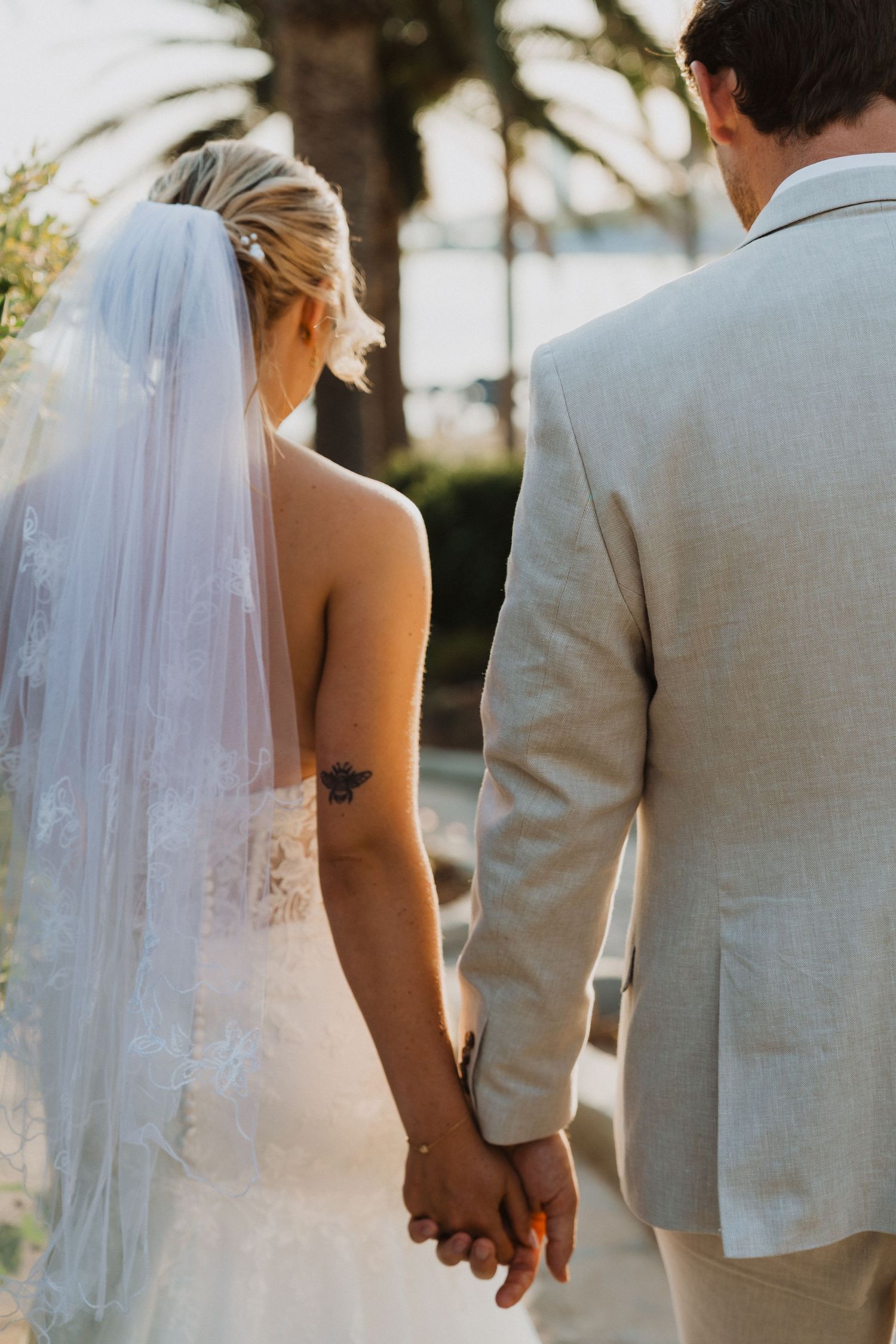 Close-up of newlyweds holding hands, showing bride's tattoo and flowing veil.