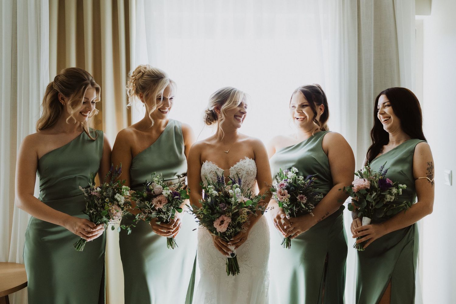 Wedding party lineup showing coordinated sage green dresses and matching bouquets.