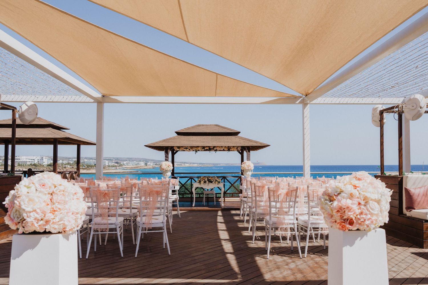 Panoramic view of a coastal wedding setup with white chairs and peach-colored decorations.